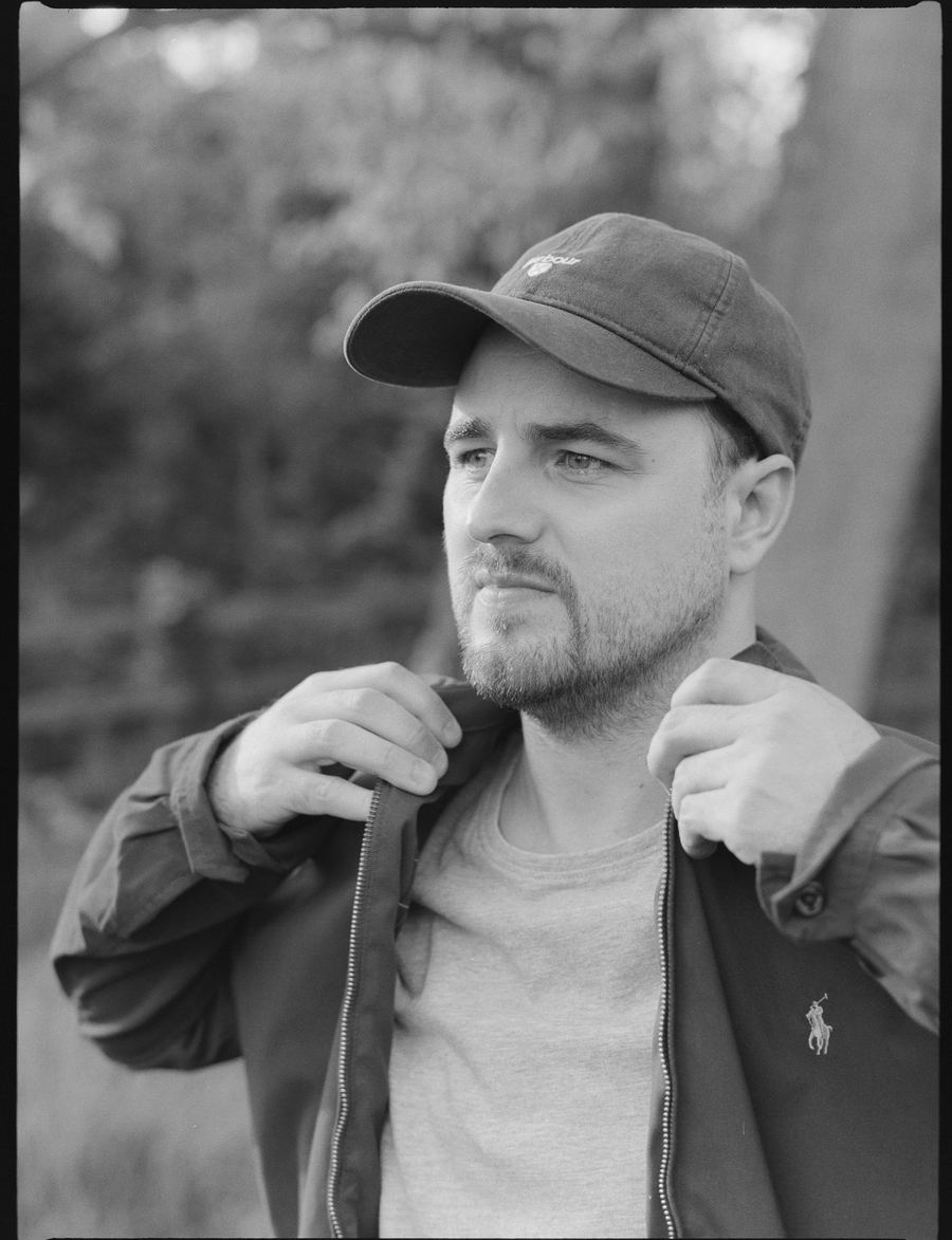 Black and white portrait of Elliott holding his jacket collar
