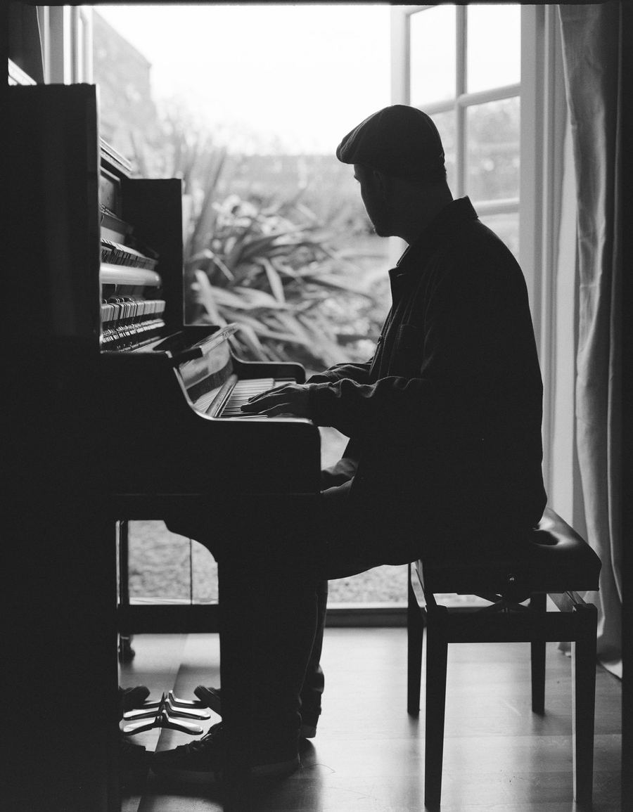 Black and white photograph of Elliott at the piano by a window