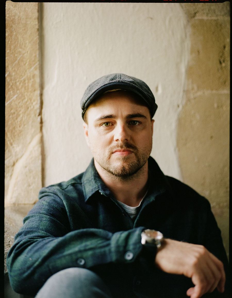 Elliott seated against a stone wall in a flat cap